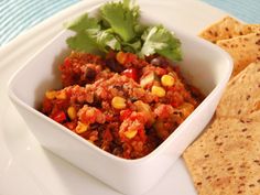 a white bowl filled with chili and corn next to tortilla chips on a plate