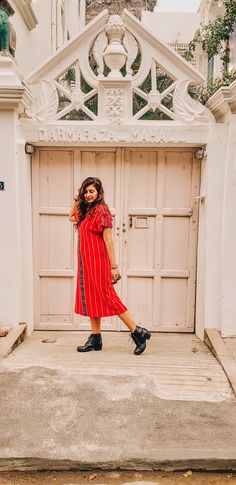 a woman standing in front of a white door wearing a red dress and black boots