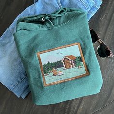 Introducing the first of our embroidered Scenic Collection, "Sasquatch Cabin"! This high detail artwork was designed and embroidered from scratch by us. Our hoodies and sweatshirts are made from high-quality fabric and feature unique embroidered designs. Whether you're looking for a stylish garment for yourself or a unique gift for a loved one, our embroidered clothing is guaranteed to satisfy! Don't forget to select a color that specifies 'Crewneck' or 'Hoodie' to choose your garment type. Hoodie 7.8 ounce, 50/50 Cotton/Polyester Fleece Air jet yarn for softness Classic fit Crewneck 8-ounce, 50/50 cotton/poly 60/40 cotton/poly (Heather Sports) Double-needle stitching at waistband and cuffs 1x1 rib knit collar, cuffs and waistband with spandex Each embroidered design is lined with soft com Vintage Long Sleeve Hoodie For Outdoor, Mountain Embroidery Hoodie, Cozy Crew Neck Hoodie For Outdoors, Cozy Outdoor Hoodie Sweatshirt, Mountain Clothes, Outdoor Graphic Print Crew Neck Sweatshirt, Camping Gift Ideas, Camping Forest, Granola Outfits