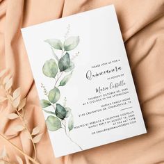 a wedding card with greenery on it sitting on top of a pink bed sheet