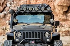 a jeep with four lights is parked in front of a rock wall and some rocks