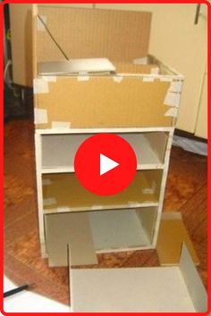 an open cardboard box sitting on top of a wooden floor next to a white shelf