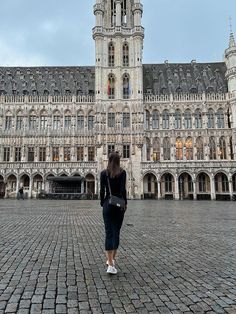 a woman walking in front of a large building with a clock on it's tower