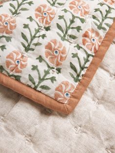 an orange and white flowered quilt on top of a bed with brown trim around the edges