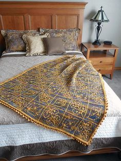 a bed with a blanket on top of it next to a night stand and lamp