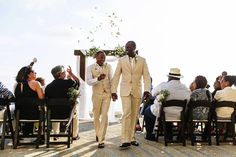 two men in suits walking down the aisle at a wedding ceremony with people sitting on chairs