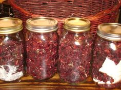 four jars filled with red flowers sitting on top of a wooden table next to a wicker basket