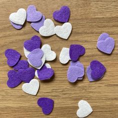 purple and white felt hearts are scattered on a wooden surface with one cut in half