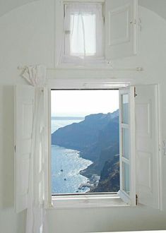 an open window in a white room with the view of mountains and water from it