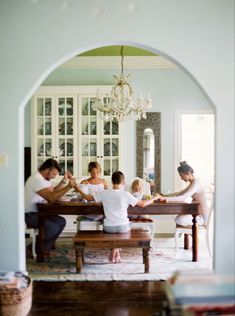 a family sitting at a dining room table in front of a chandelier and bookshelf