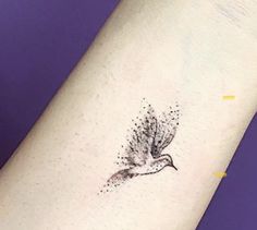 a small bird tattoo on the left inner forearm and wristband, with tiny dots all over it