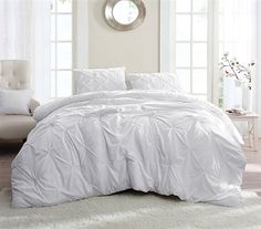 a bed with white comforter and pillows in a room next to a window,