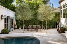 an outdoor dining area next to a pool with chairs and trees in the back yard