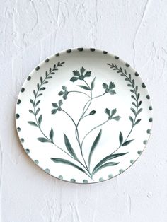 a white plate with green leaves on it hanging from the wall, against a white background