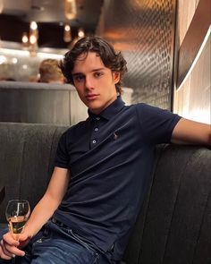 a young man sitting on a couch holding a glass of wine in front of him