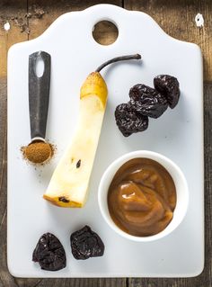 an assortment of fruits and spices on a cutting board with a knife, bowl of raisins, salt and pepper