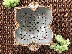 a ceramic dish sitting on top of a wicker table next to some green grapes