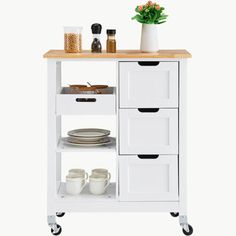 a white kitchen cart with drawers and plates on the bottom shelf next to a potted plant