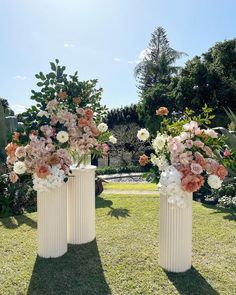 two white vases filled with flowers on top of a grass covered field next to trees