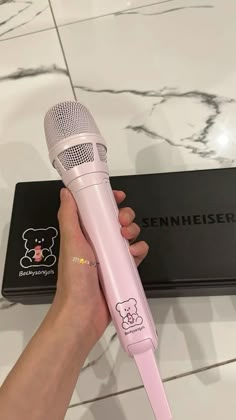 a person holding a pink microphone in front of a black box on a marble surface