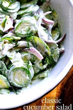 a salad with cucumbers, onions and dill is in a white bowl