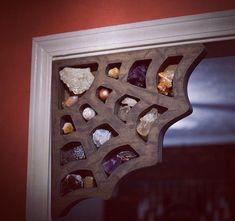 a wooden shelf with rocks and crystals in it on the side of a window sill