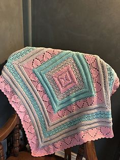 a pink and blue crocheted blanket sitting on top of a wooden rocking chair