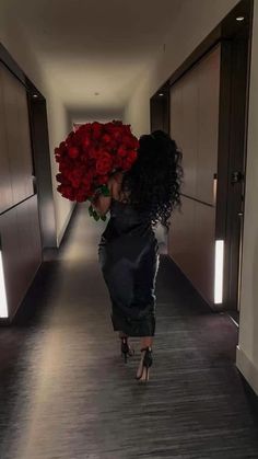 a woman walking down a hallway with red roses in her hand