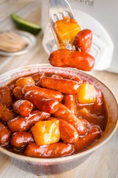 a bowl full of hot dogs and pineapples with a fork sticking out of it