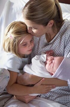 a woman holding a baby in her arms while laying on top of another woman's chest