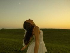 a woman in a white dress is standing in a field with her eyes closed and head tilted to the side