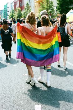 two women are walking down the street with a rainbow blanket on their shoulders and feet