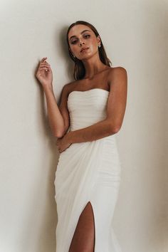 a woman in a white dress leaning against a wall with her hand on her hip