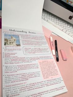 a pink desk with an open book, pen and computer keyboard on top of it