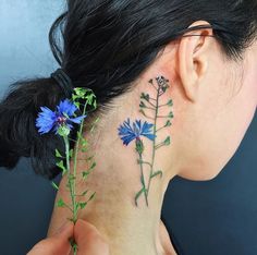 a woman with tattoos on her neck and behind her ear is a blue wildflower