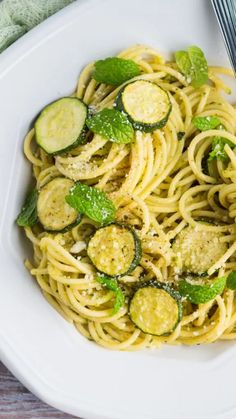 pasta with zucchini and pesto on a white plate next to a fork