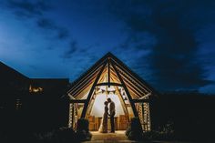 a bride and groom standing in front of a lit up gazebo