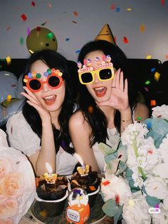 two women with party hats and sunglasses are posing for the camera in front of confetti