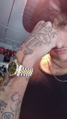 a young man with tattoos on his arm and wrist is looking at the camera while holding his hand to his face