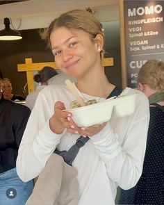 a woman holding a bowl of food in front of her face and smiling at the camera