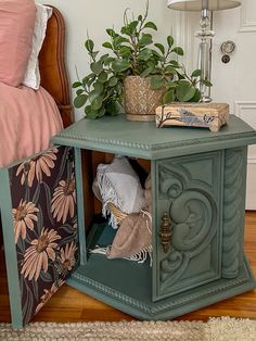 a green side table with some plants on top and a bed in the back ground