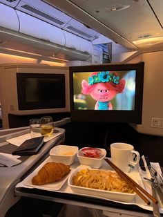 an airplane tray with food and drinks on it in front of a television screen showing the movie