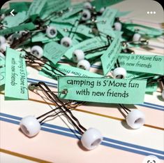 there are many pins and tags on the table that say camping is s'more fun with new friends