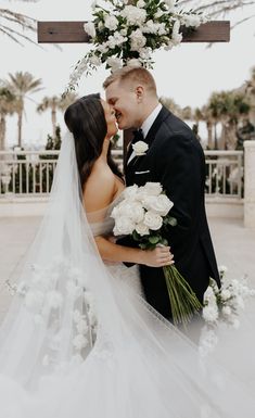 a bride and groom kissing under an arch decorated with white flowers at the end of their wedding day