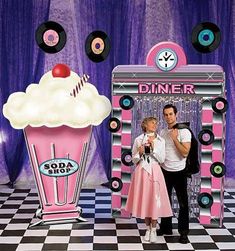 a man and woman standing in front of a pink ice cream sundae machine with donuts on top