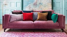 a couch with many pillows on it in front of a wall and rugs around the room