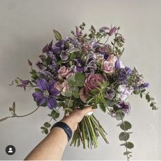 a person holding a bouquet of flowers in their hand with purple and pink blooms on it