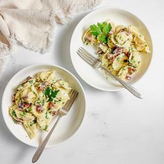 two white bowls filled with pasta and garnished with parsley on the side