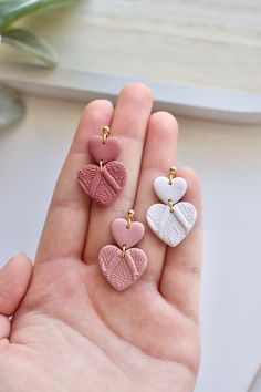 three heart shaped earrings are in the palm of someone's hand, one is pink and one is white