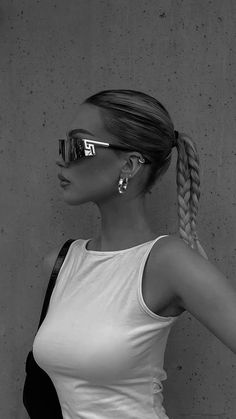 a woman with sunglasses on her head standing in front of a wall and wearing a white tank top